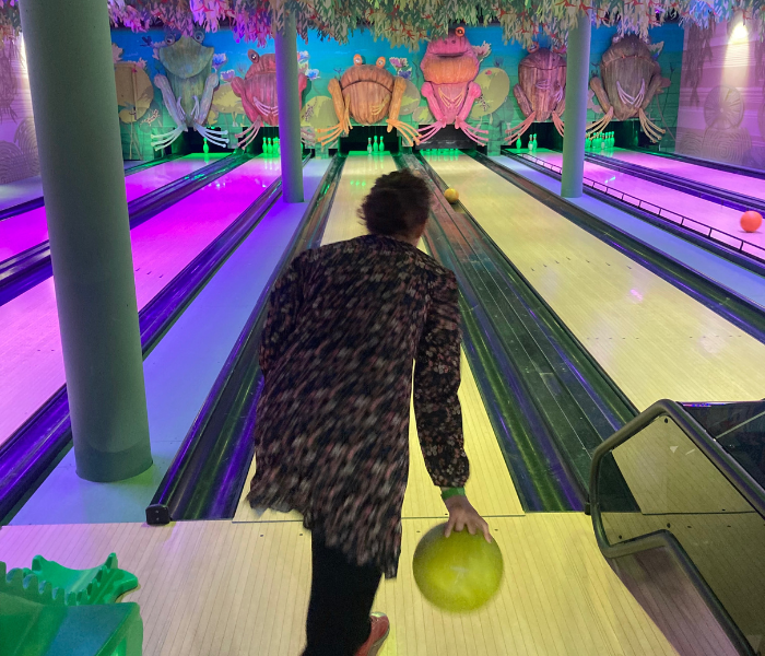 An adult enjoying a game of bowling with colourful, illuminated pins in the background during a family weekend.