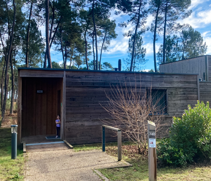 A family enjoying a stay in a modern wooden cabin surrounded by tall trees at Center Parcs Les Landes de Gascogne. Perfect for a relaxing weekend getaway in nature.