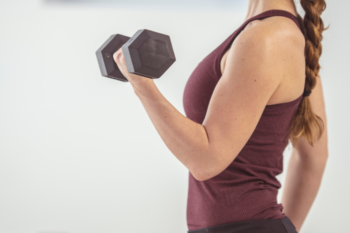 Woman lifting a dumbbell in a gym, focusing on arm strength and fitness training.