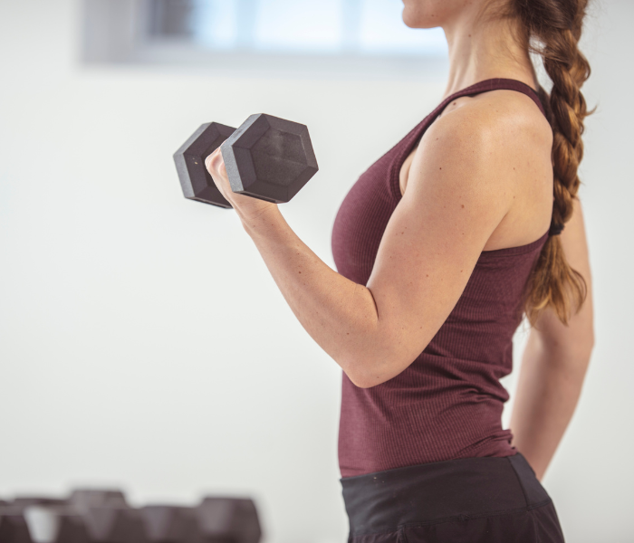 Woman lifting a dumbbell in a gym, focusing on arm strength and fitness training.