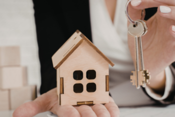 so eone holding house keys and a mini wooden house