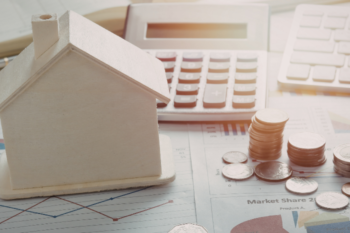 Small wooden house model placed on financial documents with coins, calculator, and charts, symbolising real estate investment and financial planning.