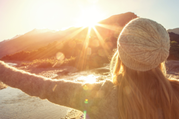 lady from the back with arms spread wide overlooking mountain and sun rise